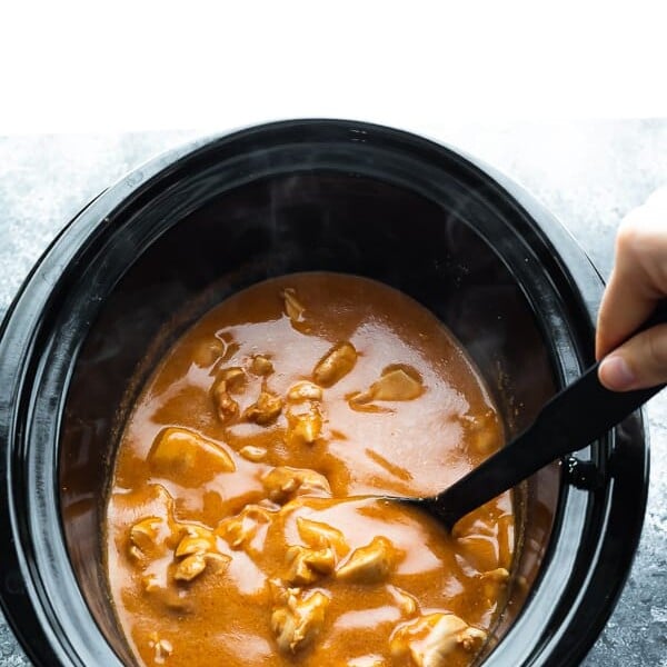 spoon stirring butter chicken in a slow cooker