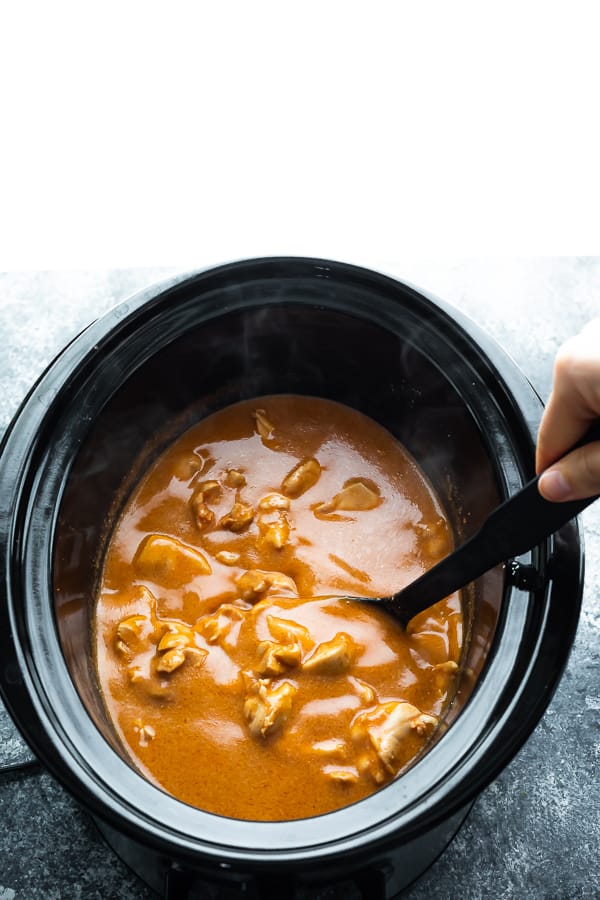 spoon stirring butter chicken in a slow cooker