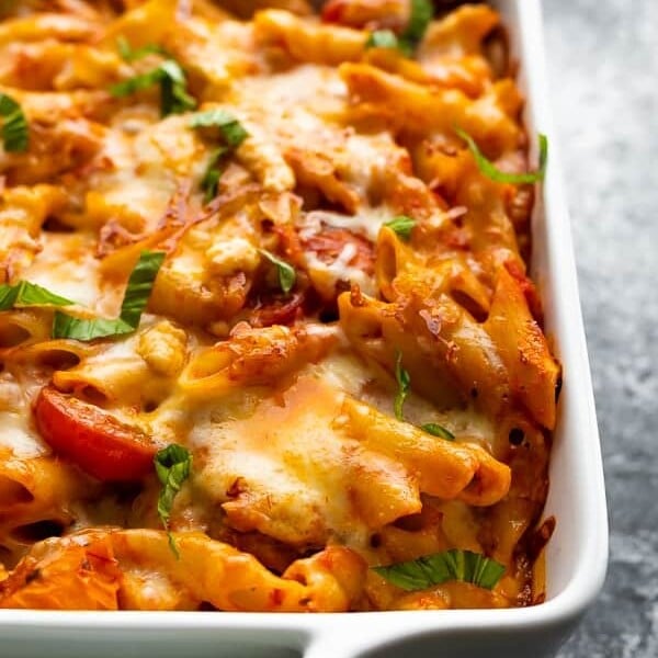 Close up shot of chicken caprese pasta bake in white casserole dish