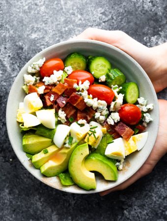 hands holding a gray bowl filled with cobb salad