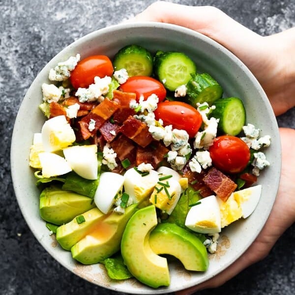 hands holding a gray bowl filled with cobb salad