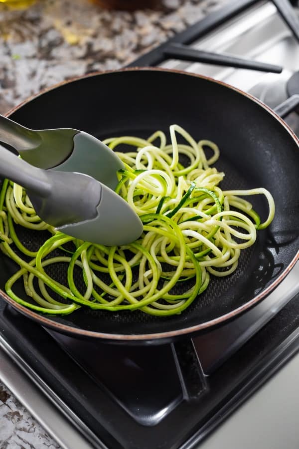 showing how to cook zucchini noodles in a nonstick skillet with tongs