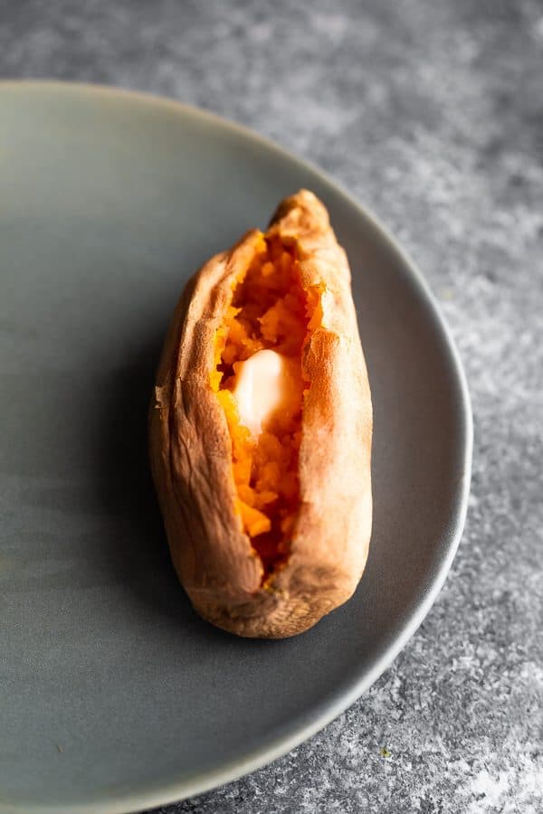 Overhead shot of a cooked sweet potato sliced open with butter on a gray plate