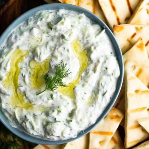 Overhead shot of tzatziki sauce in blue bowl with pita slices next to it