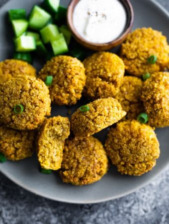 close up of a pile of crispy baked falafel on a gray plate with side of dip