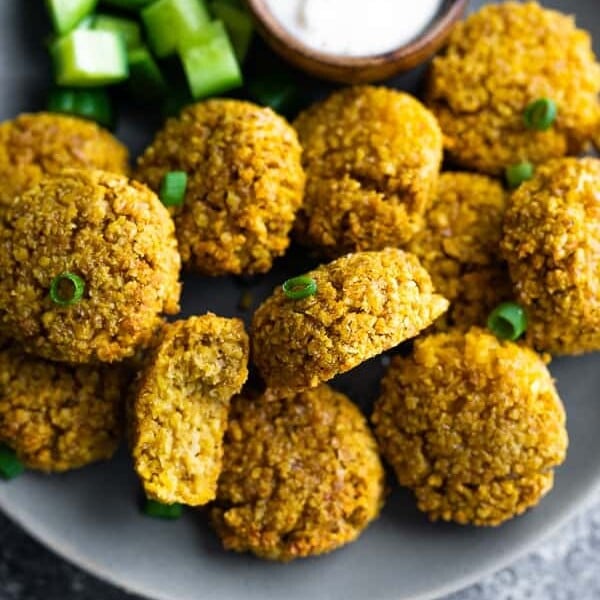 close up of a pile of crispy baked falafel on a gray plate with side of dip