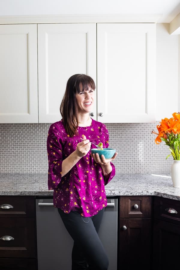 Photo of Denise standing in her kitchen eating out of a blue bowl