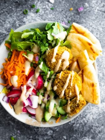 overhead shot of a falafel salad bowl with pita bread and dressing drizzled on top