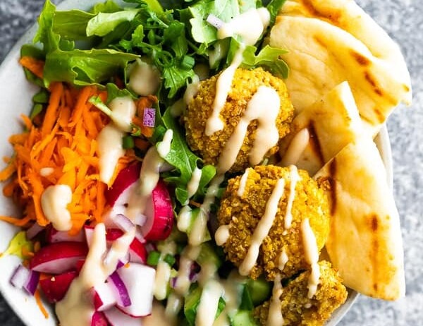 overhead shot of a falafel salad bowl with pita bread and dressing drizzled on top