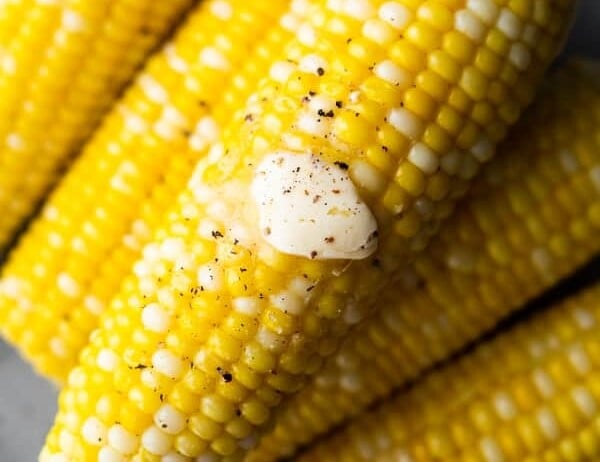 overhead shot of a pile of corn cobs with knob of butter and pepper on top
