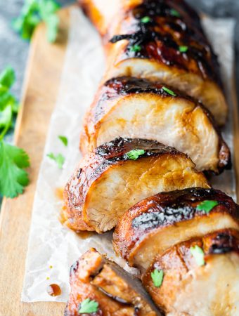 Pork tenderloin cooked with marinade and sliced on a wood cutting board with parsley in background