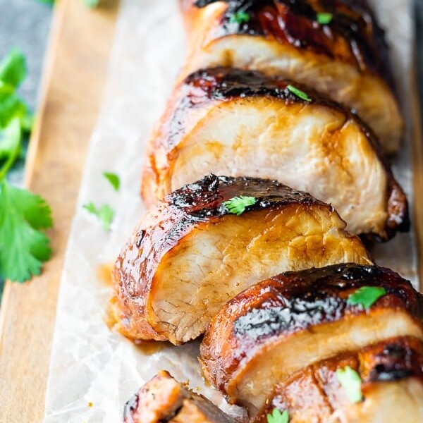 Pork tenderloin cooked with marinade and sliced on a wood cutting board with parsley in background