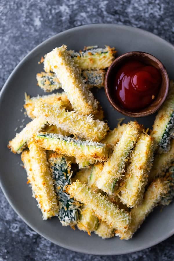 overhead shot of crispy baked zucchini fries on gray plate with small bowl of ketchup