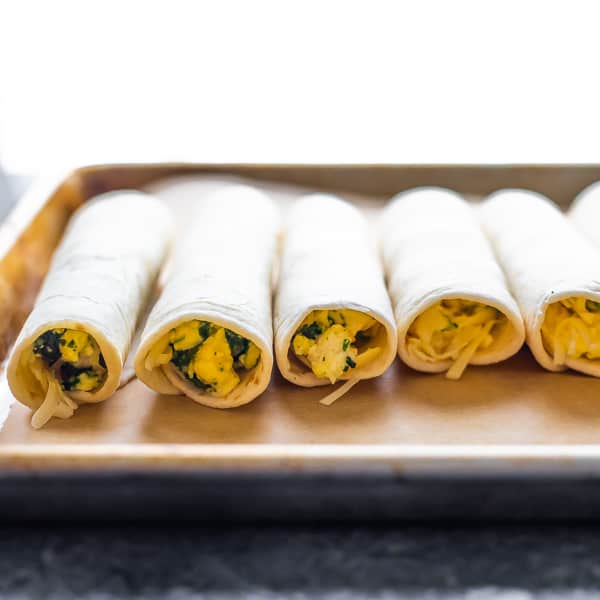 breakfast taquitos on sheet pan before baking from side view