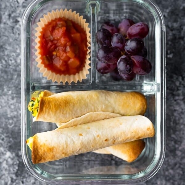 overhead shot of breakfast taquitos in a meal prep container with a side of salsa and grapes