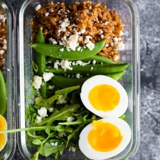 overhead shot of farro arugula salad with a soft boiled egg in glass meal prep container