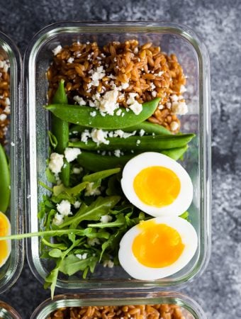overhead shot of farro arugula salad with a soft boiled egg in glass meal prep container