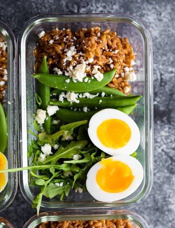 overhead shot of farro arugula salad with a soft boiled egg in glass meal prep container