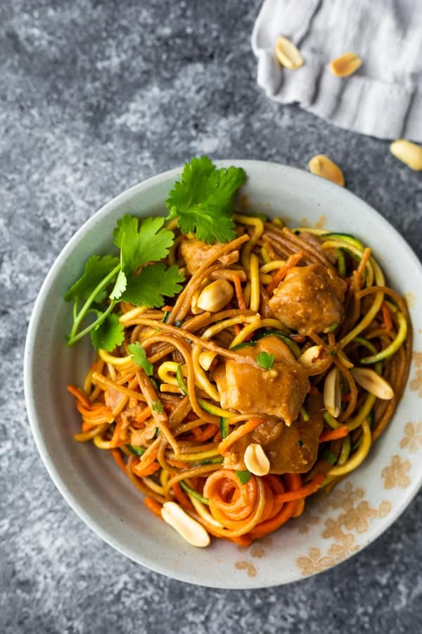 overhead shot of spicy instant pot peanut noodles in white bowl with cilantro and peanuts