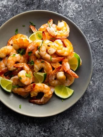 overhead shot of a pile of honey lime shrimp in gray bowl with fresh lime slices