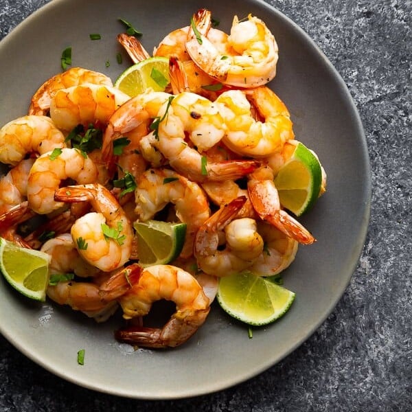 overhead shot of a pile of honey lime shrimp in gray bowl with fresh lime slices