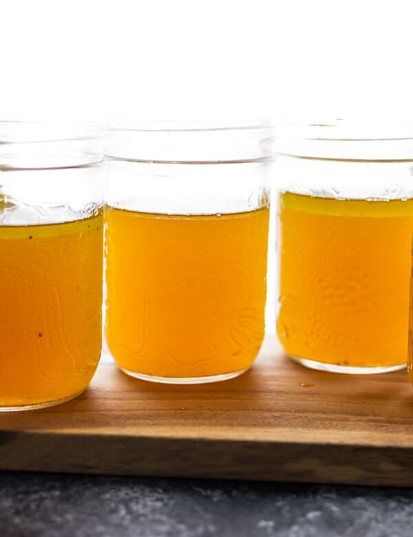 three mason jars filled with bone broth on a wood board