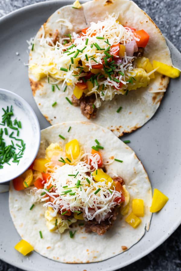 overhead shot of two breakfast tacos on a gray plate with side of sauce