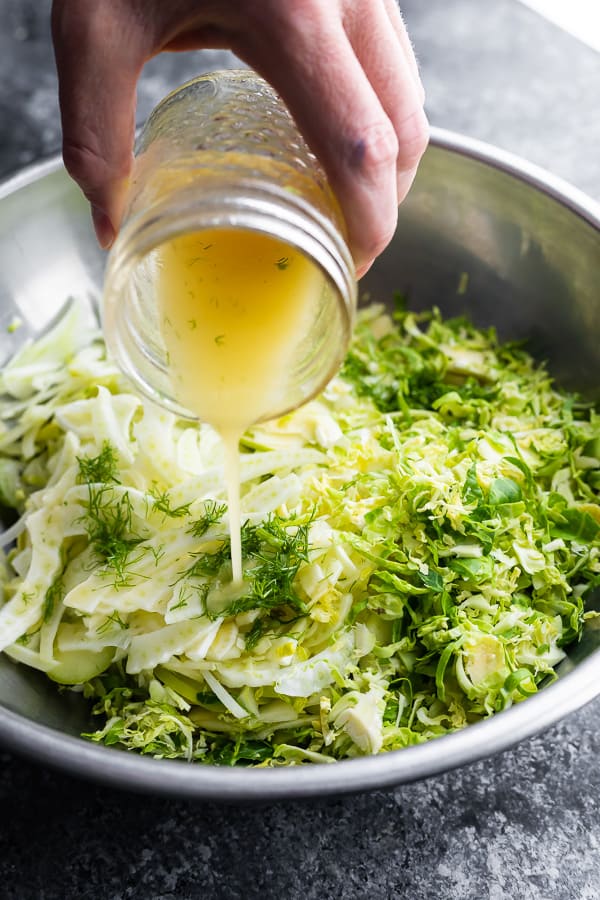 pouring the apple fennel slaw over the brussels sprouts slaw