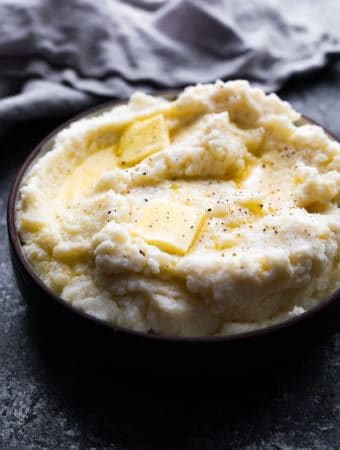 close up shot of fluffy parmesan mashed cauliflower with butter on top in black bowl
