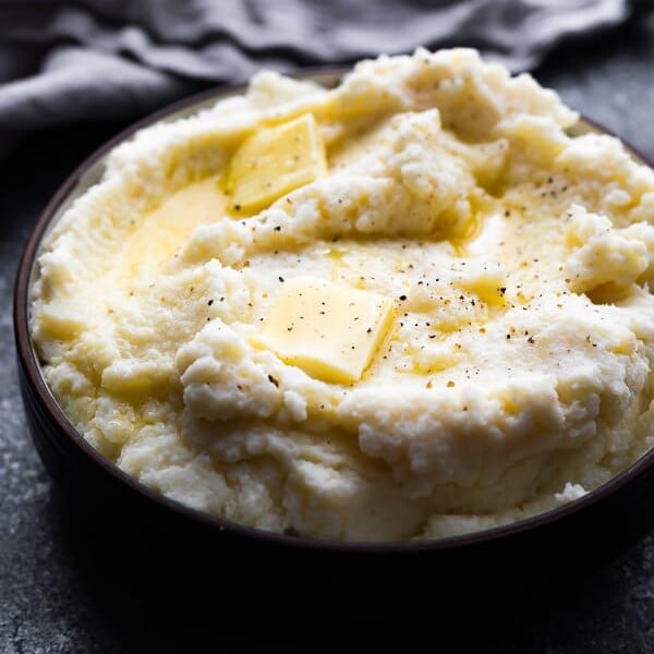 close up shot of fluffy parmesan mashed cauliflower with butter on top in black bowl