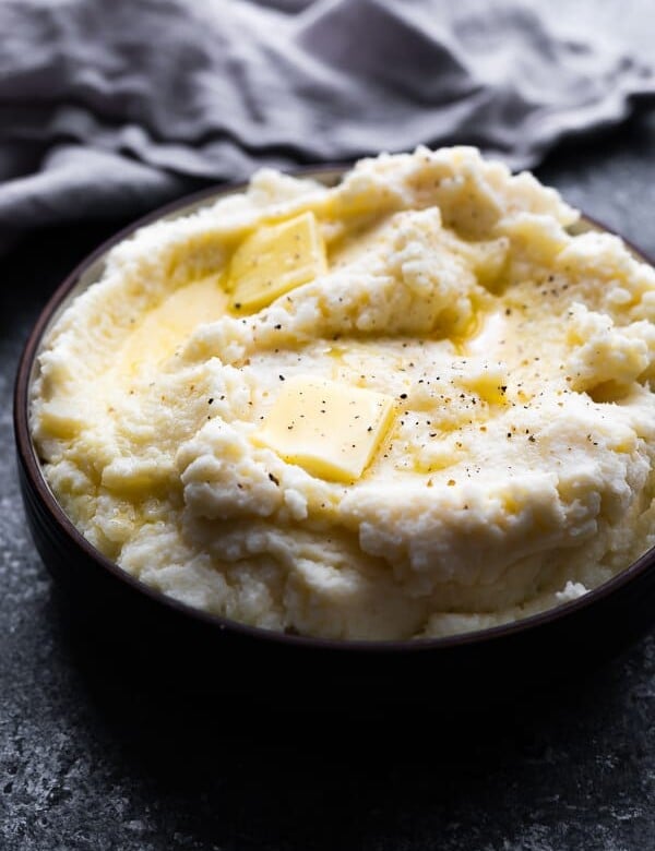 close up shot of fluffy parmesan mashed cauliflower with butter on top in black bowl