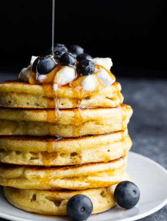 a stack of fluffy protein pancakes with blueberries on top and syrup being drizzled over them