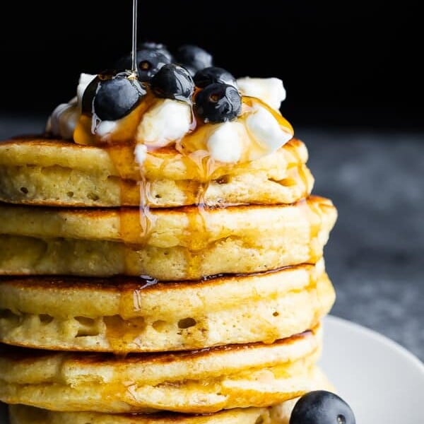 a stack of fluffy protein pancakes with blueberries on top and syrup being drizzled over them