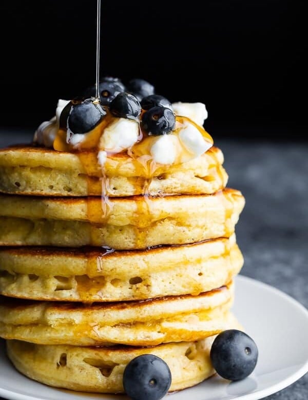 a stack of fluffy protein pancakes with blueberries on top and syrup being drizzled over them