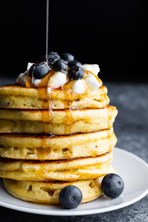 stack of protein pancakes with greek yogurt, blueberries and maple syrup drizzling