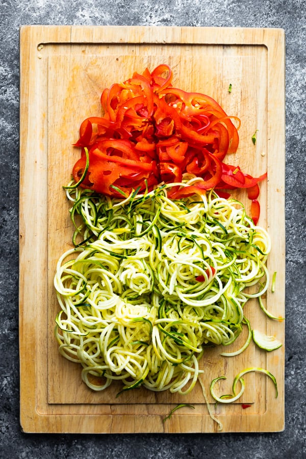 zucchini noodles and sliced red pepper on wood cutting board from overhead