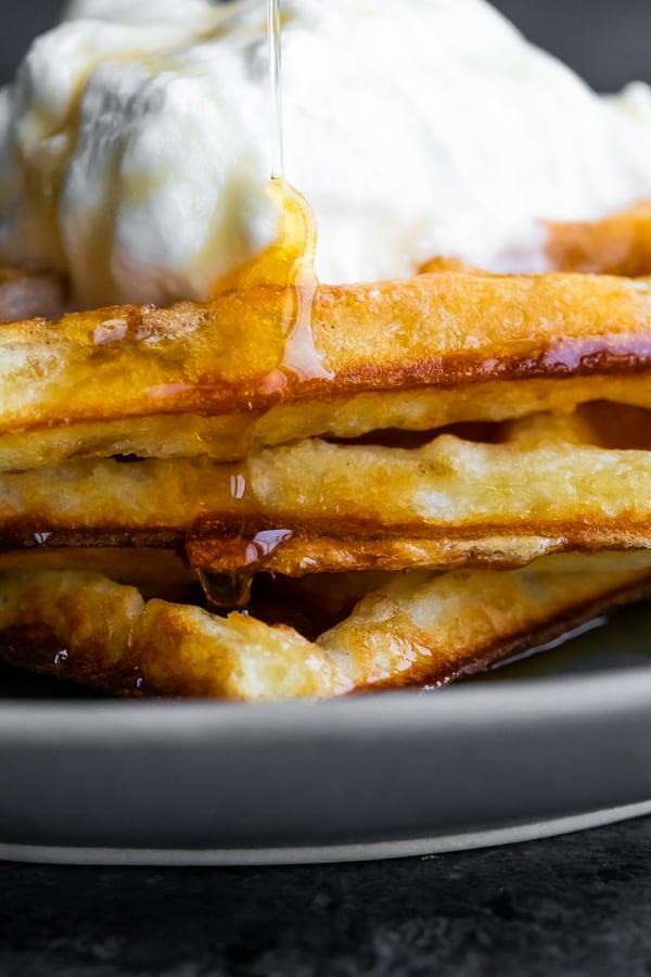 close up view of crispy waffles with syrup running down the side