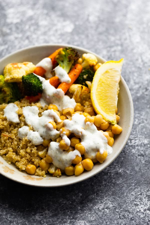 white bowl with chickpeas, roast veggies, white sauce and fresh lemon