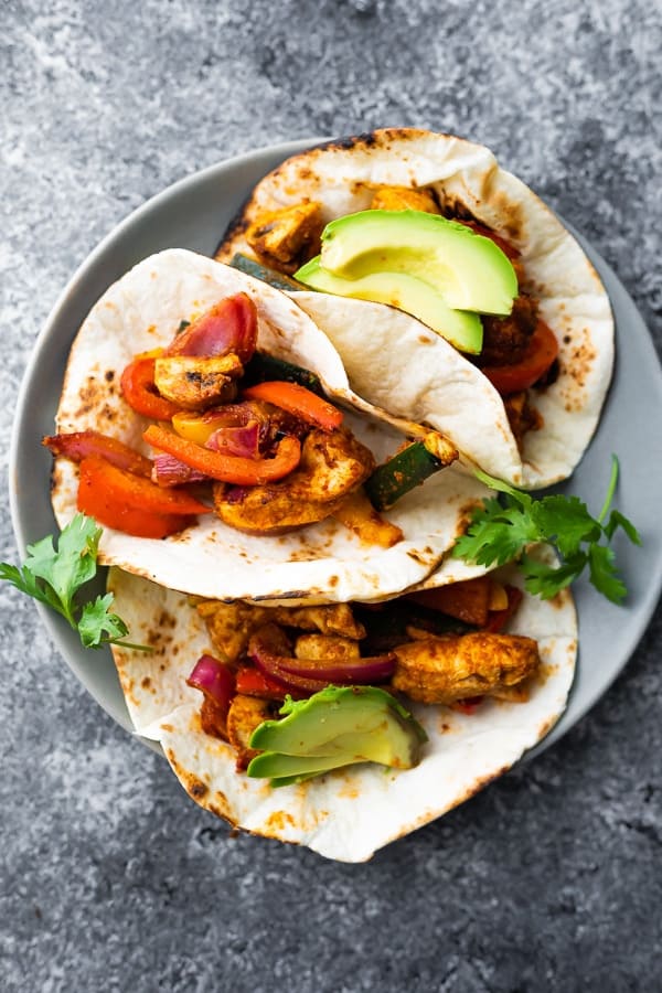 overhead view of sheet pan chicken fajitas in tortillas on plate