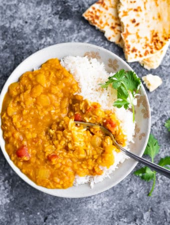 overhead shot of rice and red lentil dal in a white bowl with a fork and fresh cilantro