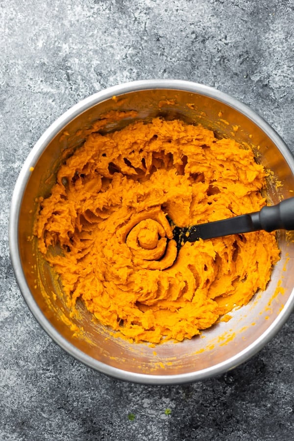 mashed sweet potato in a large metal bowl from above, with potato masher 