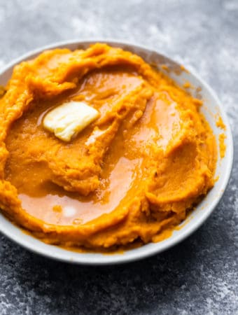 close up shot of mashed sweet potatoes with butter in a white bowl