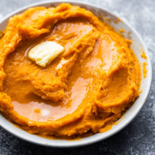 close up shot of mashed sweet potatoes with butter in a white bowl