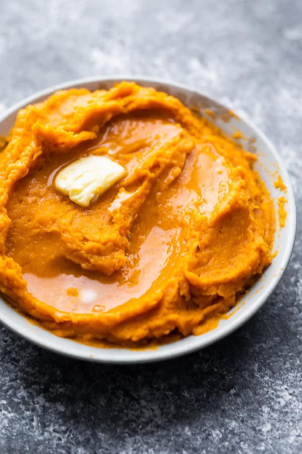 close up shot of mashed sweet potatoes with butter in a white bowl