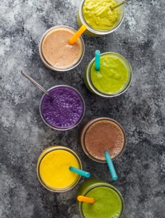 overhead shot of seven flavors of breakfast smoothies in mason jars with straws