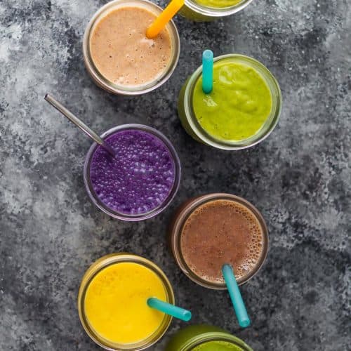 overhead shot of seven flavors of breakfast smoothies in mason jars with straws