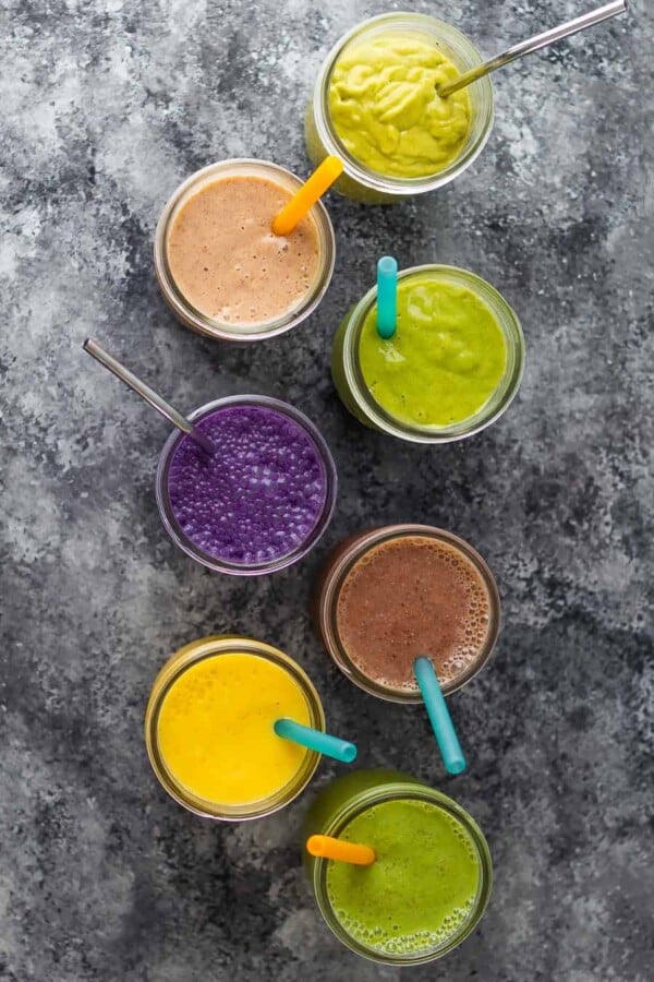 overhead shot of seven flavors of breakfast smoothies in mason jars with straws