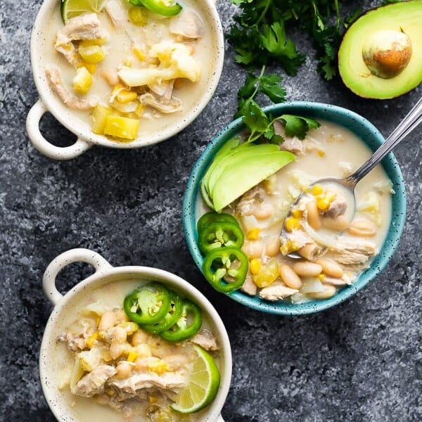 overhead shot of three white and blue bowls filled with white chicken chili and fresh avocado, lime, and jalapeno slices