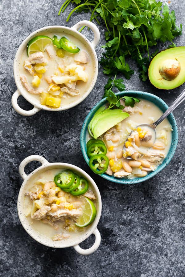 overhead shot of three white and blue bowls filled with white chicken chili and fresh avocado, lime, and jalapeno slices