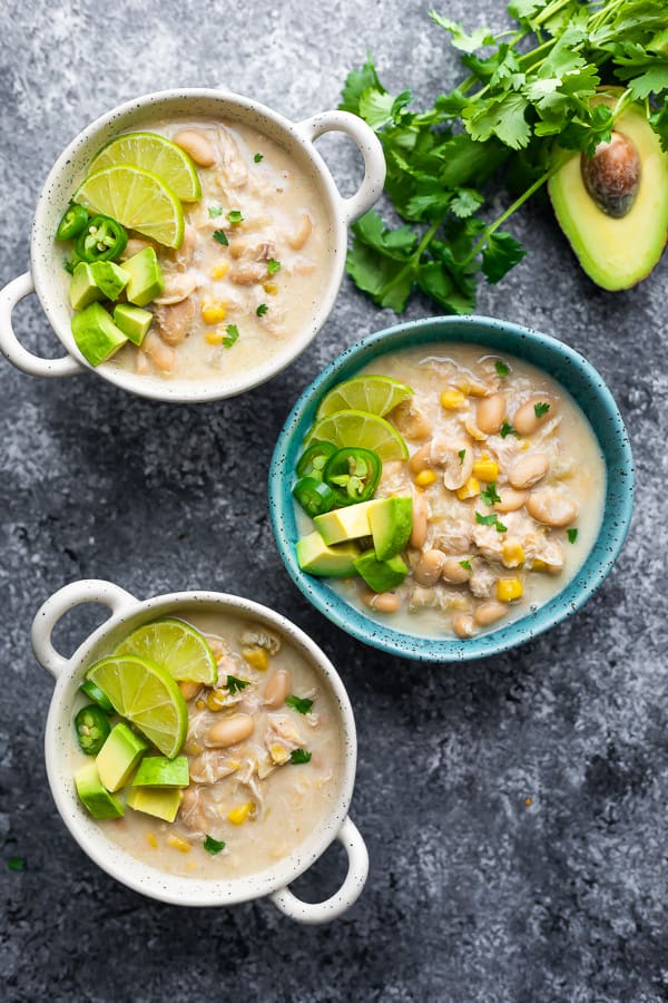 overhead shot of three bowls filled with white chicken chili with cilantro and half avocado next to bowls